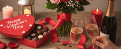 Romantic Valentine's Day champagne toast with hands holding glasses, bouquet of pink/red roses, heart-shaped chocolate box, lit candles, handwritten love notes, rose petals – free AI image